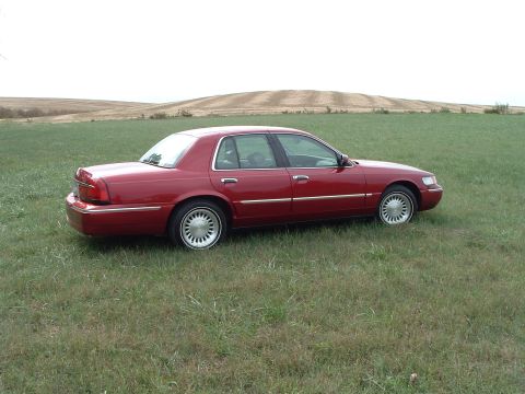 1999 Mercury Grand Marquis - A red 1999 Mercury Grand Marquis is parked in a grassy field under a cloudy sky.