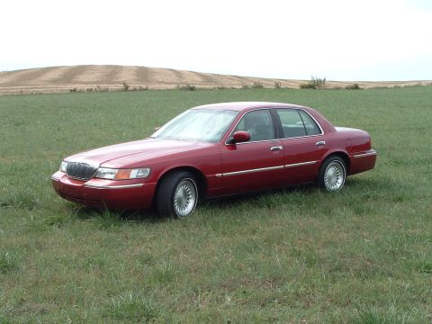 1999 Mercury Grand Marquis - A red 1999 Mercury Grand Marquis sits in a field under an overcast sky.