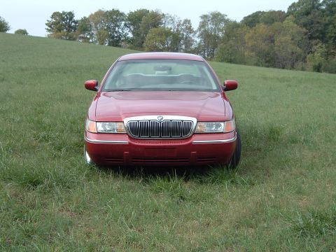 1999 Mercury Grand Marquis - A red sedan sits in a field, its front grille and headlights clearly visible.