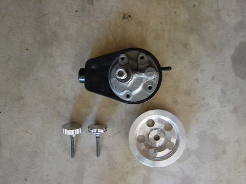 1983 Ferrari Enzo - A power steering pump, two knobs, and a pulley are laid out on a concrete floor.