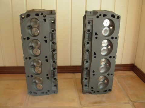 1994 Ford Bronco - A pair of engine cylinder heads are displayed on a tiled floor against a paneled wall.