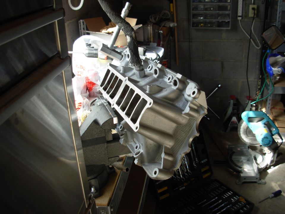 Engine intake manifold held in a vise, with tools and a chop saw in the background