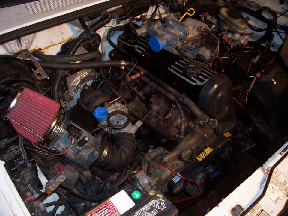 Engine bay with aftermarket red air filter, black valve covers, and visible belts and alternator