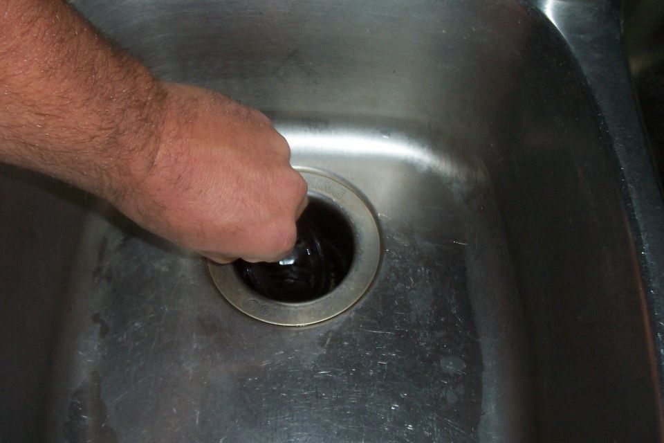 Hand reaching into a stainless steel sink drain