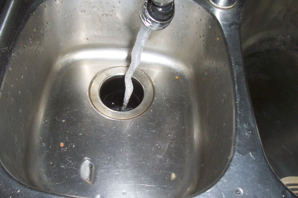 Stainless steel kitchen sink with water running from faucet into drain