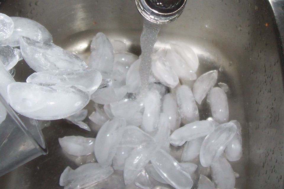 Ice cubes being rinsed in a sink with water running from a faucet