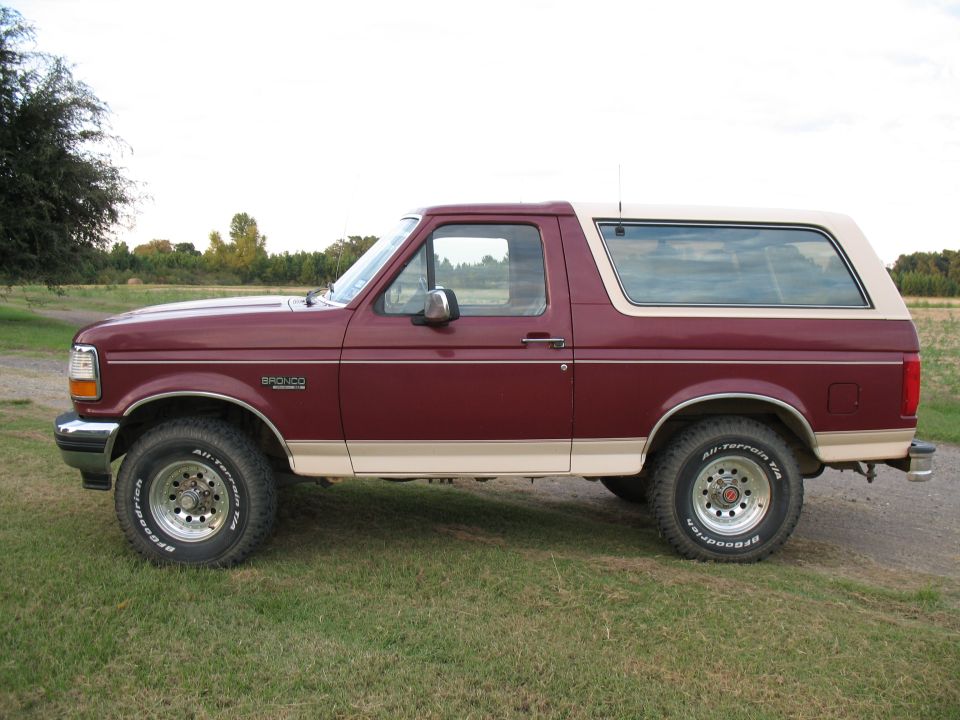 Maroon and tan two-tone Ford Bronco, side view on grass