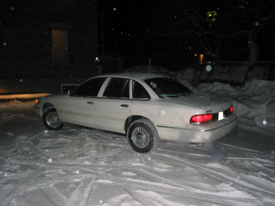 White sedan parked in snow, 3/4 front view. Visible taillight and side profile