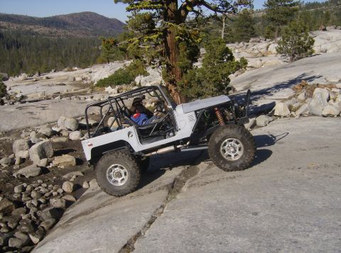 1986 Ford Bronco - Off-road vehicle navigating a rocky terrain with a mountainous backdrop.