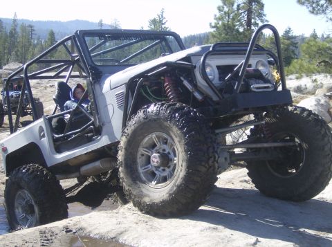 1986 Ford Bronco - A modified off-road vehicle tackles a challenging rocky path with another vehicle visible in the background.