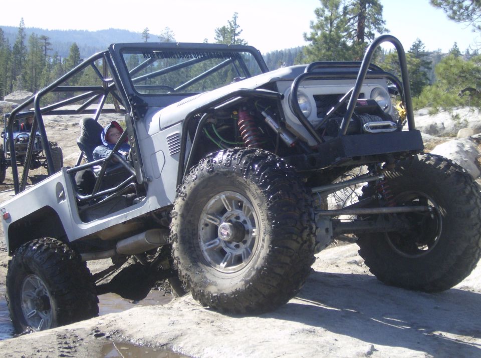Gray off-road vehicle with a roll cage, large tires, and custom suspension, navigating rocky terrain