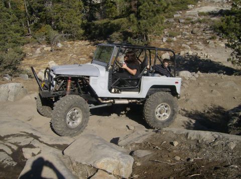 1986 Ford Bronco - This heavily modified vehicle navigates a rocky trail with two occupants inside.
