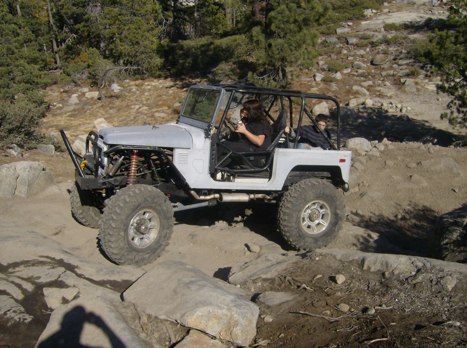 Off-road SUV with a roll cage driving over rocks. It has large tires and exposed suspension components