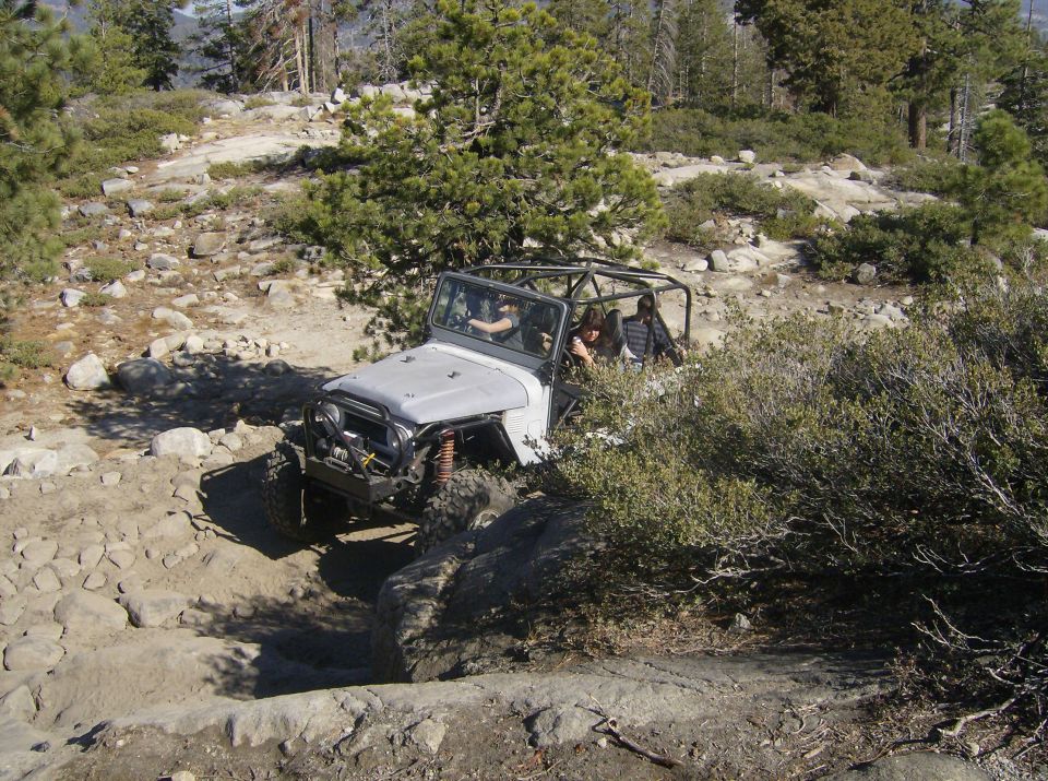 Silver off-road vehicle with a roll cage navigating a rocky trail