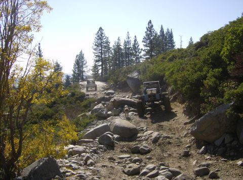 1986 Ford Bronco - Two off-road vehicles traverse a challenging, rocky mountain path, their off-road capabilities.