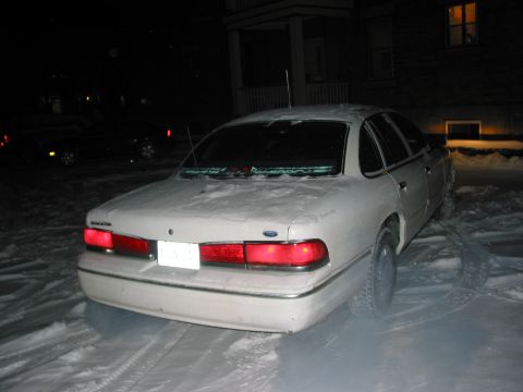 1996 Ford Crown Victoria - A white Ford Crown Victoria is parked in the snow at night, with tire tracks visible.