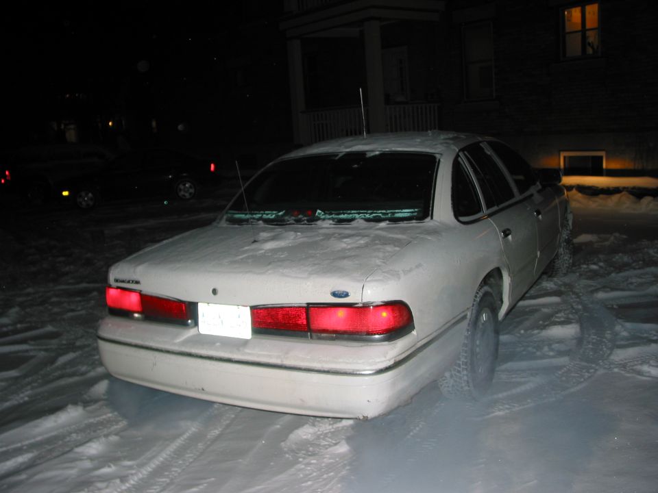 Rear of a white Ford Crown Victoria parked in snow at night
