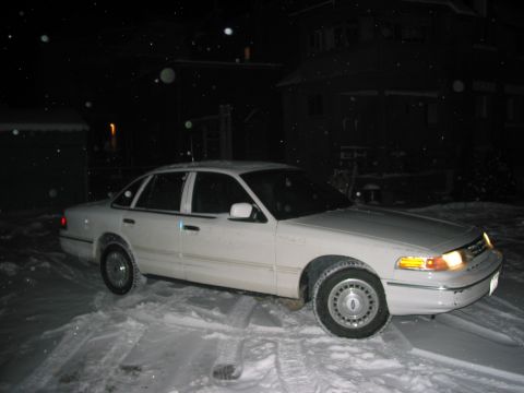 1996 Ford Crown Victoria - A white sedan sits in the snow at night, with a house in the background.