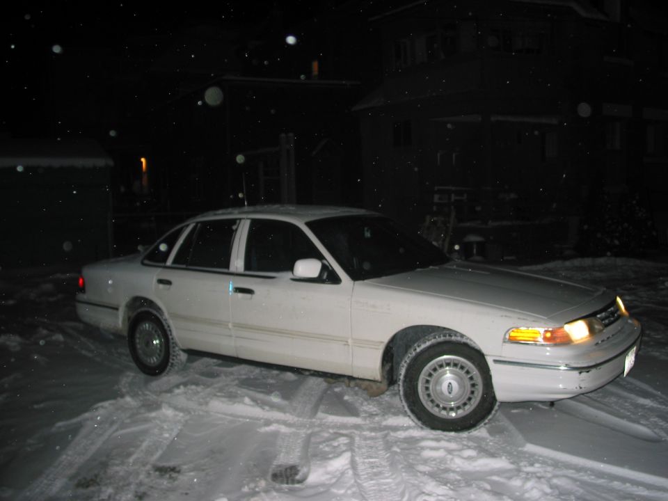 White sedan parked in snow, 3/4 front view. Visible grille and headlights