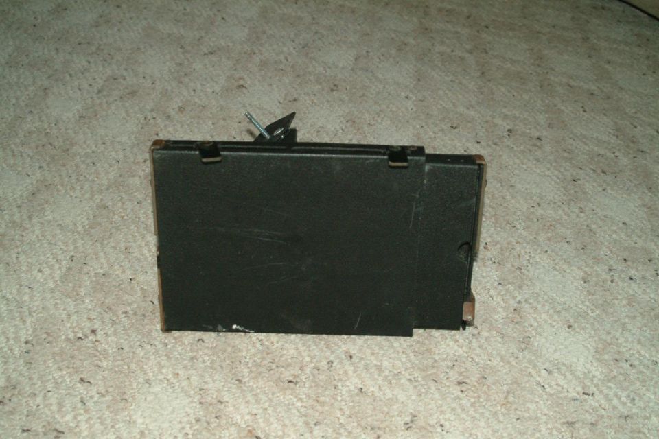 Black rectangular car part with a metal clip on top, resting on a carpeted surface