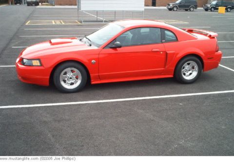 2004 Ford Mustang - Red 2004 Ford Mustang coupe with aftermarket wheels parked in a lot.