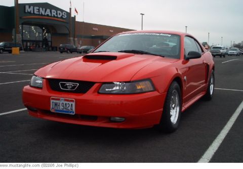 2004 Ford Mustang - A red 2004 Ford Mustang coupe is parked in a lot with a Menards store in the background.