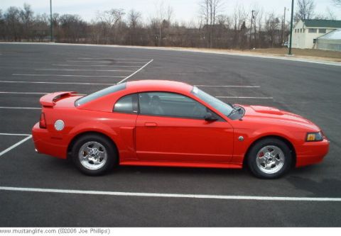 2004 Ford Mustang - A red 2004 Ford Mustang coupe is parked in an empty lot under an overcast sky.