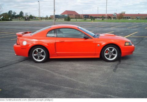 2004 Ford Mustang - This orange 2004 Ford Mustang coupe is shown from the side in a parking lot.