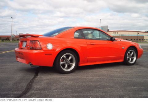 2004 Ford Mustang - Rear quarter view of an orange 2004 Ford Mustang coupe parked in a lot.