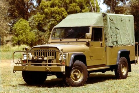 1991 Ford Bronco - Olive drab military truck with canvas top and brush guard parked in a grassy field.
