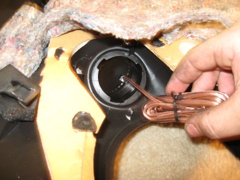 2002 Pontiac Trans Am - A hand holds copper speaker wire near an open speaker housing within a vehicle's interior.