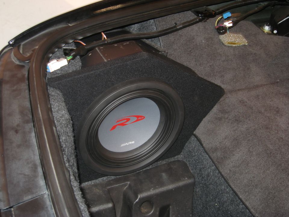 Alpine subwoofer installed in car trunk, with wiring visible