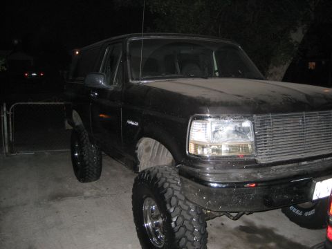 1993 Ford Bronco - This black Ford Bronco features a significant lift kit and aggressive off-road tires, viewed from a three-quarter front angle at night.