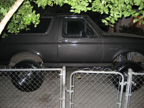 1993 Ford Bronco - This lifted 1993 Ford Bronco features a dark gray exterior and is parked behind a chain-link fence.