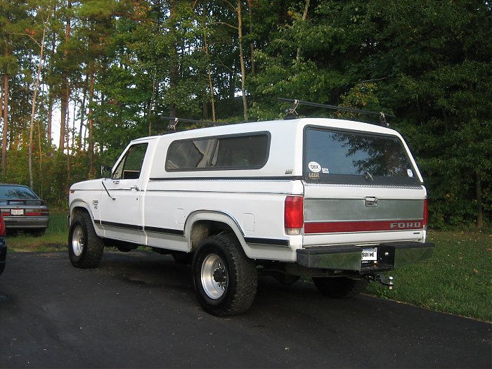 White 1980s Ford pickup with matching Leer topper, roof rack, and black tube rear bumper