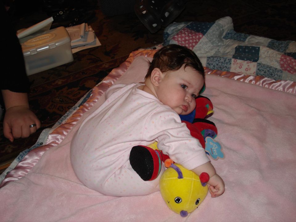 Baby in pink pajamas lying on a pink blanket with stuffed toys