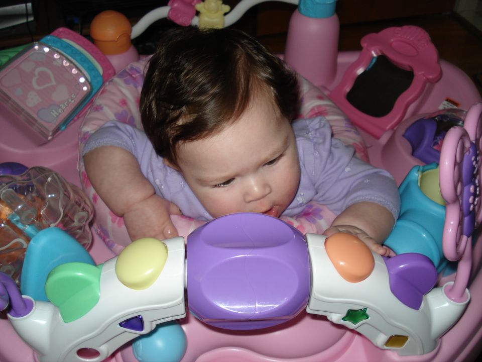 Baby in a pink play seat with colorful toys