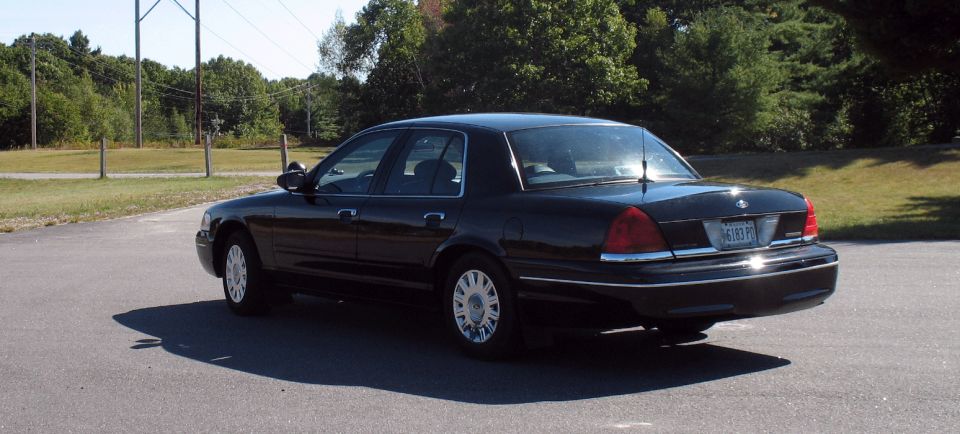 Dark sedan parked on a paved surface with trees in the background