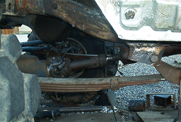 Underside of a vehicle showing the drive shaft, leaf springs, and suspension components