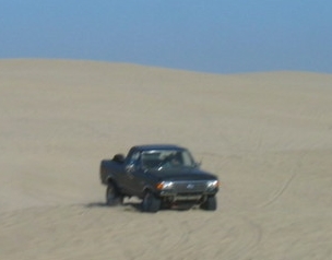 1989 Ford Bronco - Ford pickup truck navigates sandy terrain on a clear day.