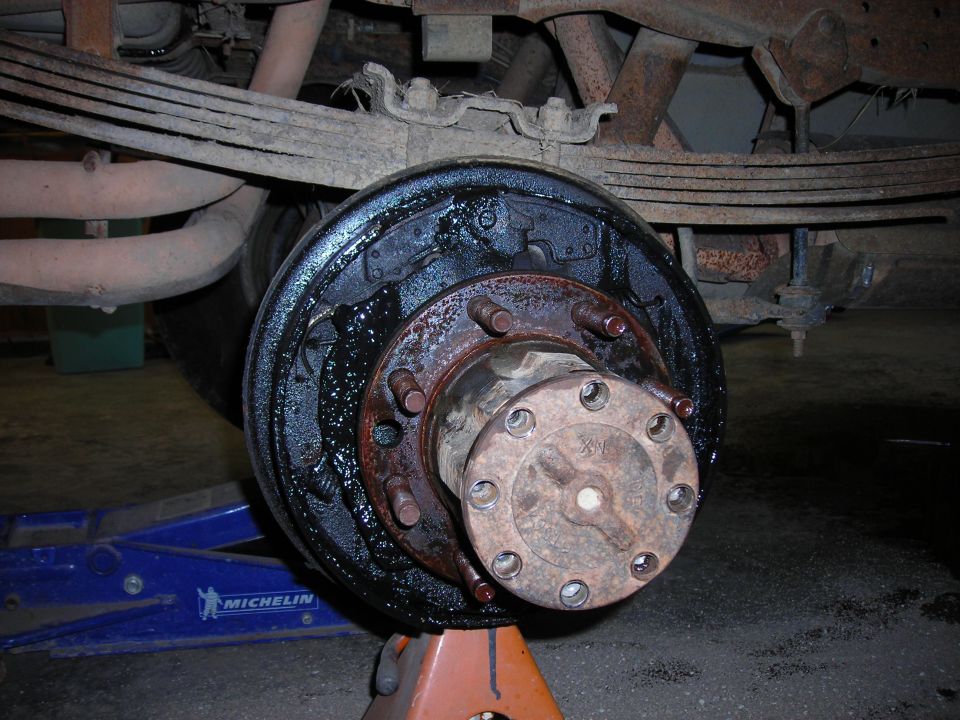 Exposed rear brake hub and backing plate covered in grease, on jack stand
