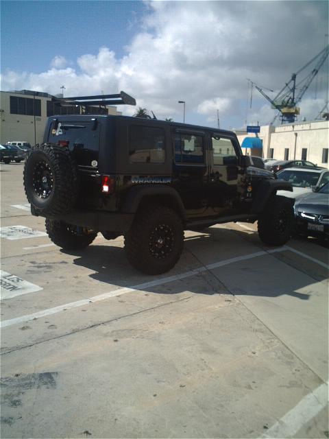 1994 Ford Bronco - A black Jeep Wrangler is parked outdoors, a prominent rear spoiler and a spare tire mounted on the tailgate.