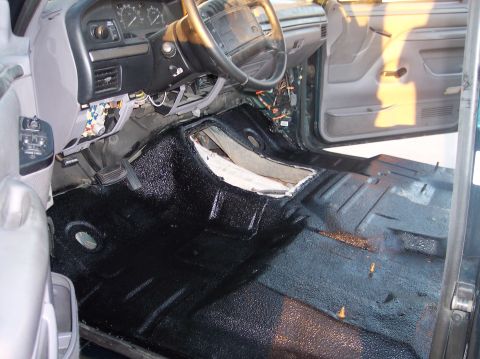 1995 Ford Bronco - The interior of a Ford Bronco shows a dark green dashboard and door panels with the floor coated in black spray-on bedliner.