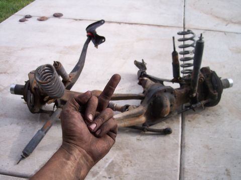 1995 Ford Bronco - Disassembled suspension components lie on concrete, with a dirty hand giving the middle finger obscuring part of the view.