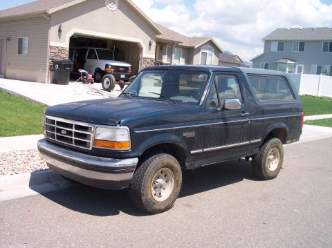 1995 Ford Bronco - A dark blue Ford Bronco is parked on the street in front of a house with an open garage.