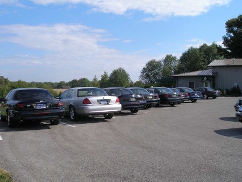 1998 Ford Crown Victoria - Row of Panther-platform Mercury sedans parked rear-in at a rural winery lot, most in black with MARAUDER decklid lettering and dual chrome…