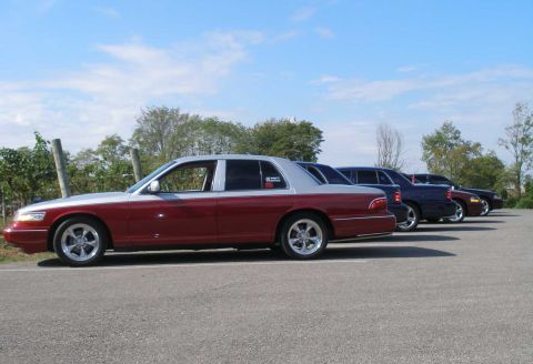 1998 Ford Crown Victoria - A two-tone maroon and silver full-size sedan is parked at an angle in a paved lot, shown from the driver's side with polished multi-spoke c…