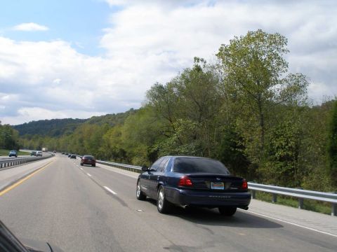 1998 Ford Crown Victoria - Rear three-quarter rolling shot of a dark blue Mercury Marauder sedan on a divided highway, with MARAUDER lettering stamped in the rear bum…