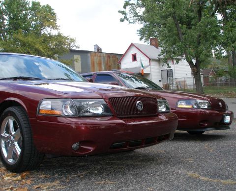1998 Ford Crown Victoria - Low front angle of two dark toreador red Mercury Marauder sedans parked side by side, showing their vertical-bar Mercury grilles, smoked he…