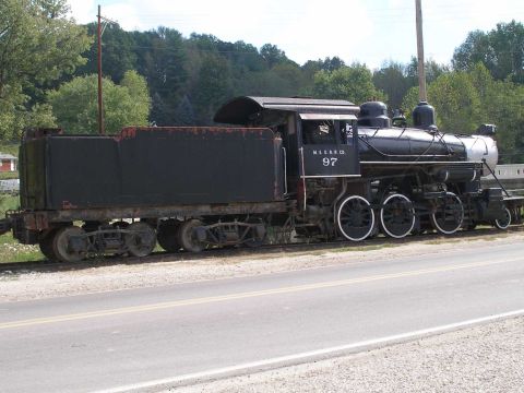 1998 Ford Crown Victoria - Black steam locomotive number 97, lettered "M. & G. R.R. CO." on its tender, displayed on a short section of track beside a two-lane road w…